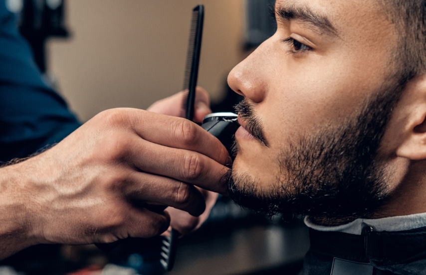 man receiving a beard trim with an electric shaver in a barbershop, highlighting precise grooming with professional tools.