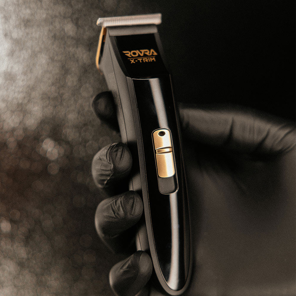 Cordless professional hair trimmer held in gloved hand with sleek black and gold design
