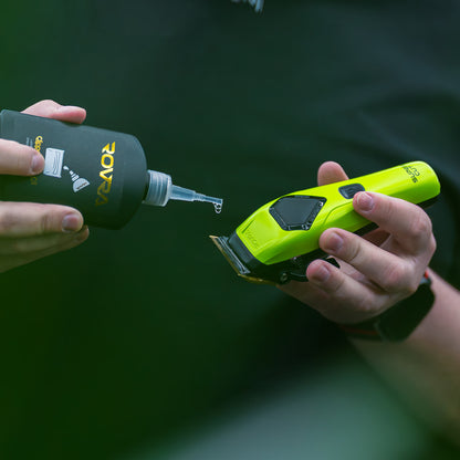 Applying professional clipper oil to a green electric hair clipper for smooth performance